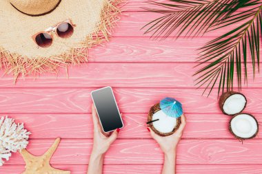 kadeh kokteyl smartphone ve Hindistan cevizi pembe ahşap yüzeyde tutan kadın kırpılmış
