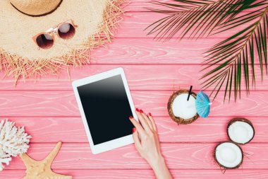 kırpılan bardak Hindistan cevizi kokteyl ve hasır şapka ile pembe ahşap yüzeyde tablet kullanan kadın