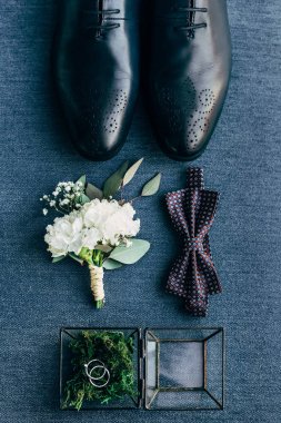 flat lay with arrangement of grooms shoes, bow tie, corsage and wedding rings for rustic wedding on blue background clipart