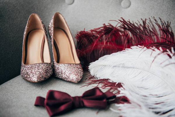 close up view of bridal shoes, grooms bow tie and feathers for rustic wedding on armchair