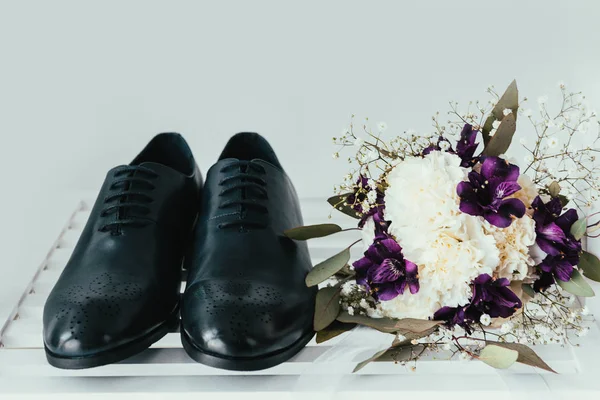 close up view of grooms shoes and bridal bouquet on grey background