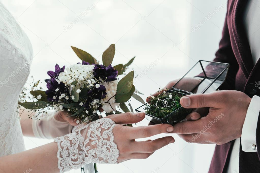 partial view of groom with wedding rings and bride with wedding bouquet in hands