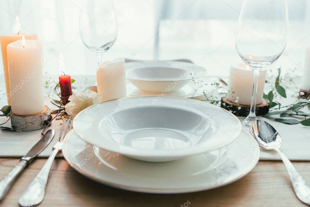 close up view of stylish table setting with candles, empty wineglasses and plates for rustic wedding