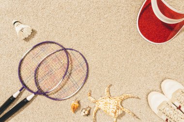kum üzerinde badminton ekipman, Ayakkabı, şapka ve deniz kabuklarını Üstten Görünüm 