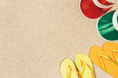 flat lay with colorful flip flops and caps arranged on sand clipart