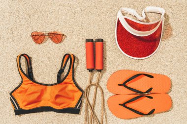 Düzenlenmiş atlama ipi, spor giyim, güneş gözlüğü, kap ve flip flop kum üzerinde Üstten Görünüm