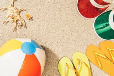 flat lay with colorful flip flops, beach ball, seashells and caps arranged on sand clipart
