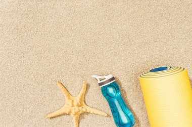 kum üzerinde sarı mat, su şişesi ve deniz yıldızı Üstten Görünüm