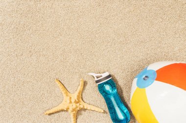 flat lay with arranged water bottle, sea star and beach ball on sand clipart