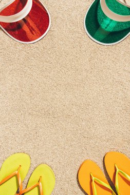 top view of arranged colorful caps and flip flops on sand clipart