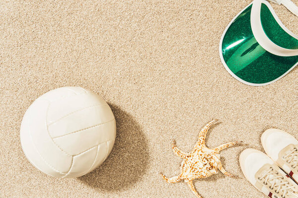 flat lay with volleyball ball, cap, sneakers and sea star on sand