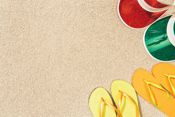 flat lay with colorful flip flops and caps arranged on sand