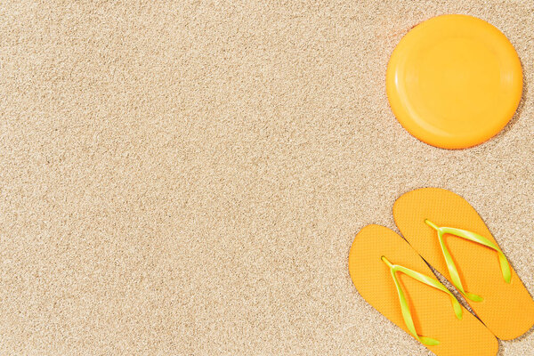 top view of yellow flip flops and frisbee on sand