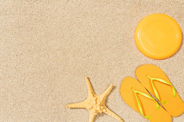 top view of sea star, yellow flip flops and flying disk on sand