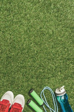 Yeşil çimenlerin üzerinde görücü usulü su şişesi, ip atlama ve spor ayakkabı Üstten Görünüm