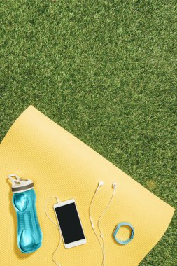 su şişesi, izle, smartphone ve yeşil çim üzerinde sarı mat kulaklıklar ile düz lay