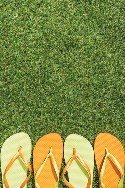 top view of green and orange flip flops on green lawn