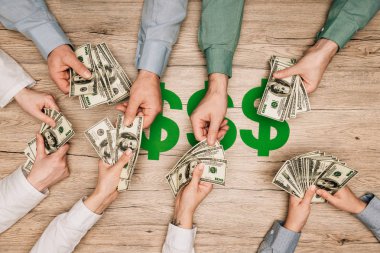 İş ortaklarının elinde dolar banknotları, masasında dolar tabelaları, kırpılmış manzarası olan...