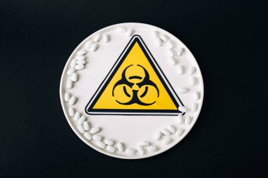 Top view of plate with pills and biohazard symbol isolated on black clipart