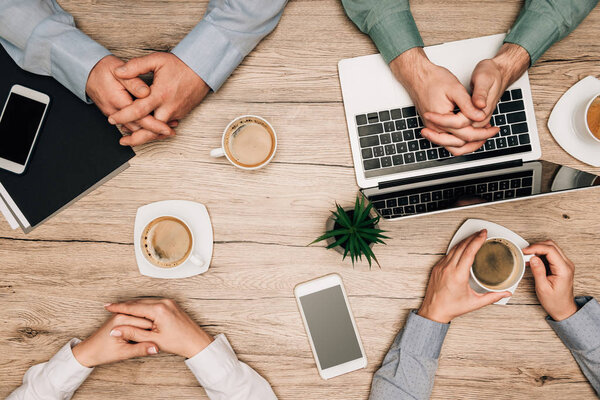 Top view of business people drinking coffee with laptop, smartphones and documents on table