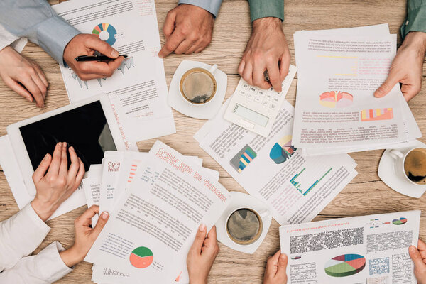 Вид сверху деловых людей, работающих с документами и цифровой табличкой за чашкой кофе на столе
