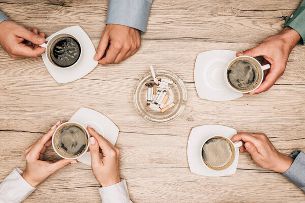 Вид сверху на бизнесменов, пьющих кофе рядом с пепельницей на столе, обрезной вид
