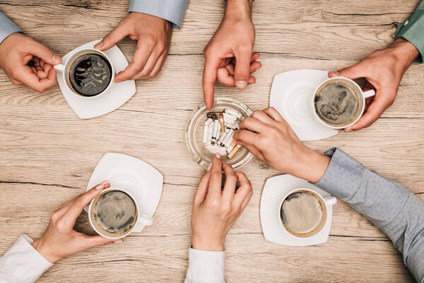 Top view of businesspeople drinking coffee and smoking at table, cropped view