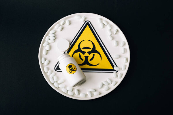 Вид надписи "Биологическая опасность" на тарелке с таблетками и бутылкой с ядовитой надписью, изолированной на черном
