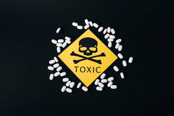 Top view of pills and toxic sign isolated on black