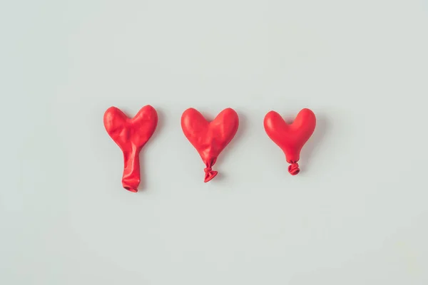 Vista superior de tres globos desinflados en forma de corazón aislados en concepto de día de San Valentín blanco - foto de stock