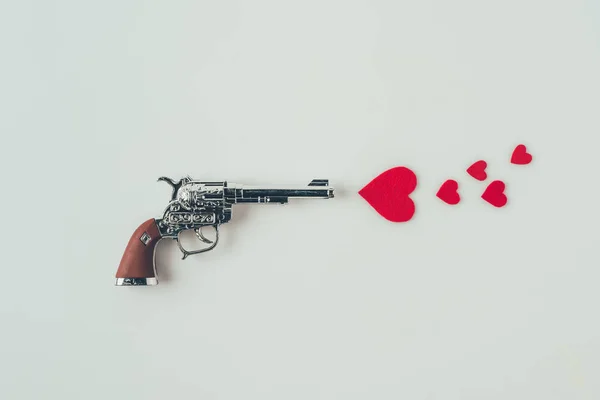 Vista superior de la pistola apuntando a corazones de papel aislados en el concepto de día de San Valentín blanco - foto de stock