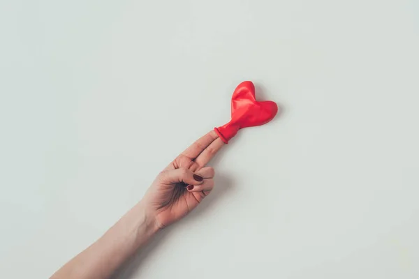 Imagem cortada de balão em forma de coração em dois dedos femininos em branco, conceito dia dos namorados — Fotografia de Stock