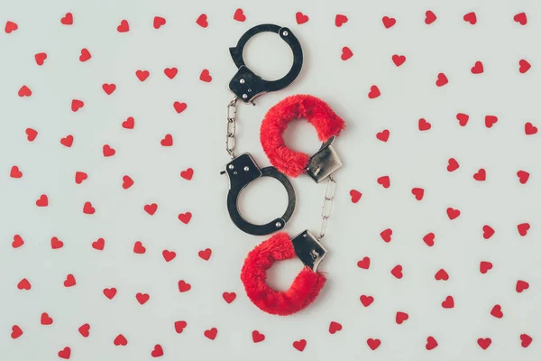 Top view of black and red handcuffs with scattered paper hearts isolated on white, valentines day concept — Stock Photo