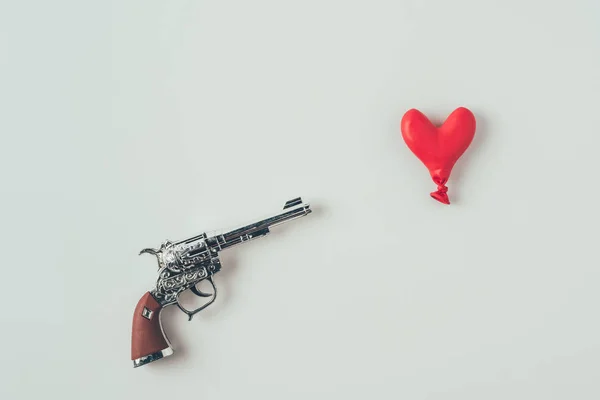 Vista superior del cañón de la pistola apuntando a globo en forma de corazón aislado en blanco, concepto de día de San Valentín - foto de stock