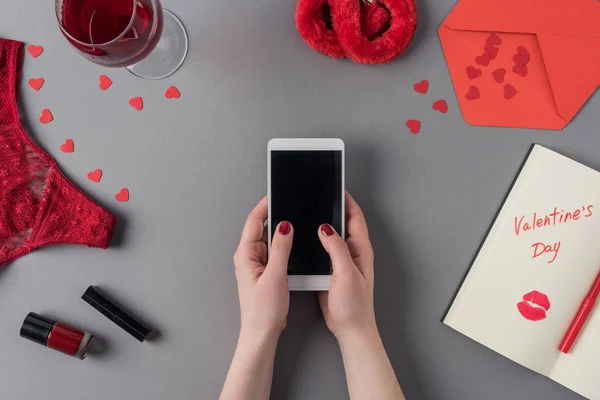 Imagen recortada de la mujer sosteniendo el teléfono inteligente en las manos, portátil con palabras día de San Valentín - foto de stock