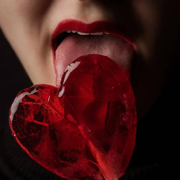 Imagen recortada de mujer lamiendo paleta en forma de corazón aislado en negro, concepto de día de San Valentín - foto de stock