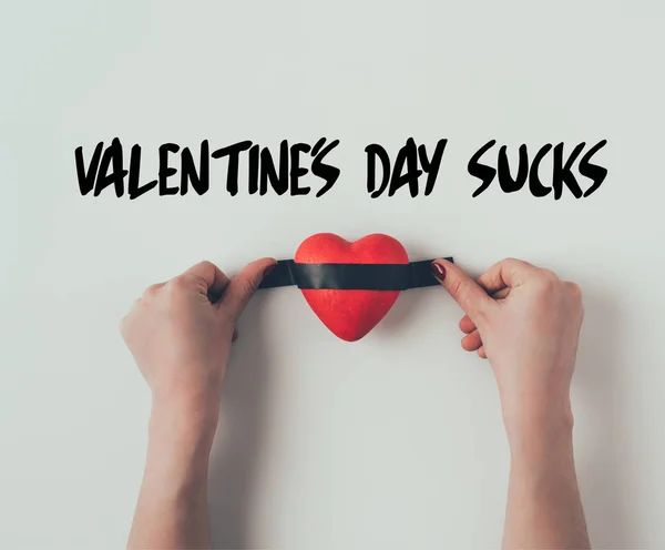 Cropped image of woman putting insulating tape on red heart and words valentines day sucks on white — Stock Photo