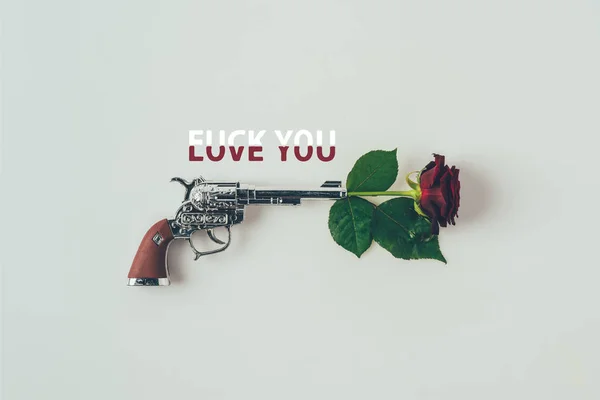 Vista superior de rosa roja en cañón de pistola con palabras amor te follan aislado en blanco - foto de stock