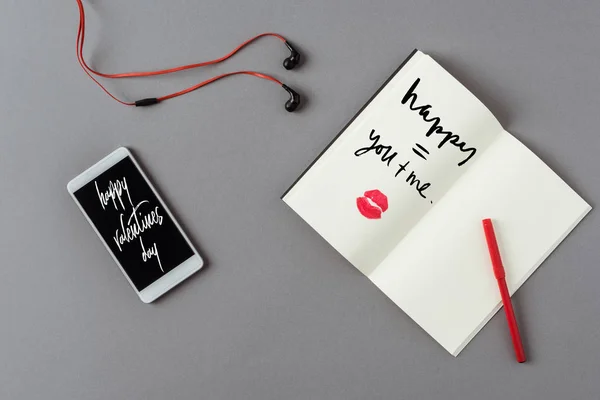 Top view of smartphone with words happy valentines day and notebook with lips print on gray surface — Stock Photo