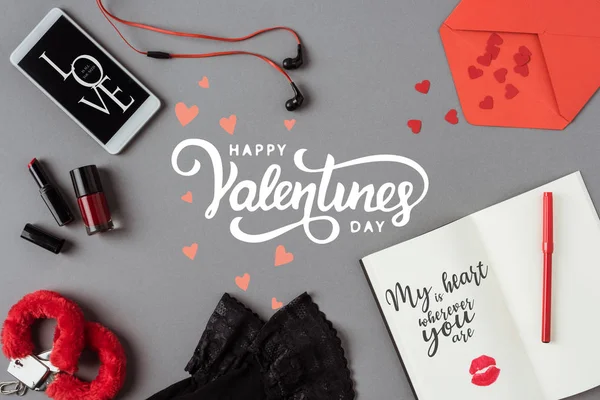 Top view of words happy valentines day between smartphone and notebook on gray surface — Stock Photo