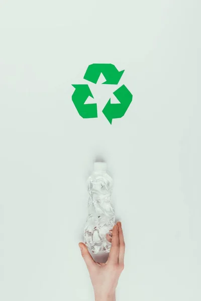 Vista parcial de una mujer sosteniendo una botella de plástico con un cartel de reciclaje aislado en gris - foto de stock