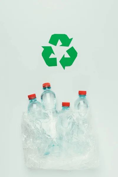 Вид зверху на знак переробки і пластикові пляшки в пластиковому пакеті ізольовані на сірому — стокове фото