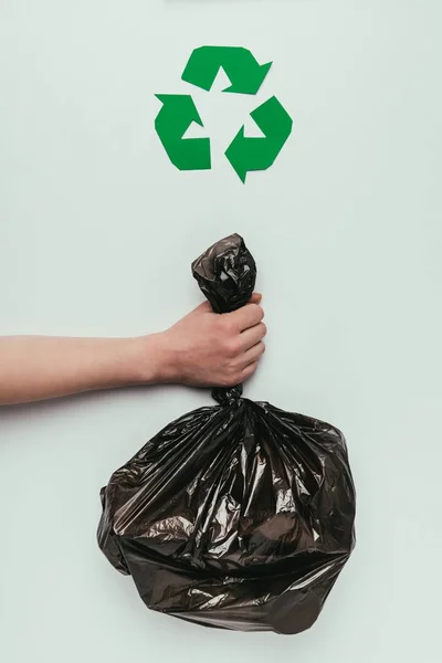 Tiro recortado de mujer sosteniendo bolsa de basura en la mano con el cartel de reciclaje aislado en gris - foto de stock