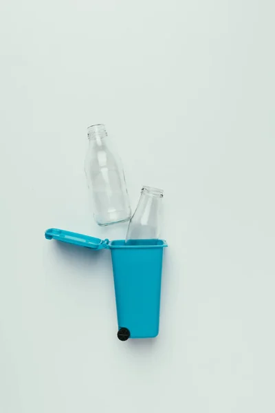 Верхний вид мусорного ведра со стеклянными бутылками, изолированными на сером, концепция переработки — стоковое фото
