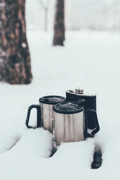 Vista ravvicinata di termotazze e fiaschetta nella neve nella giornata invernale nel bosco — Foto stock