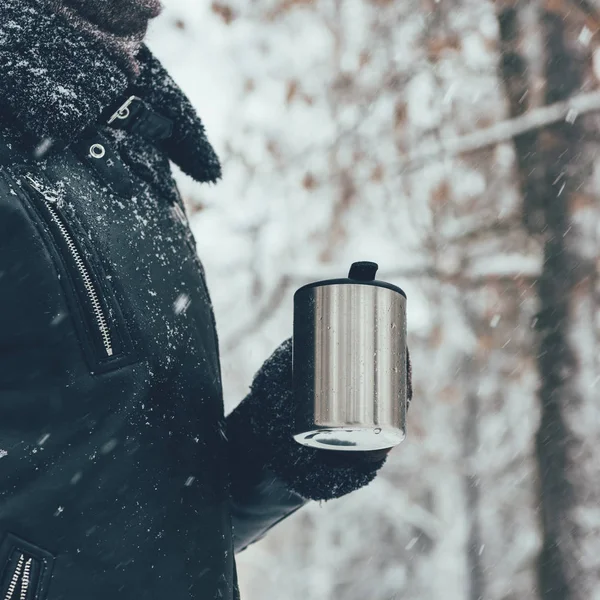 Partial view of woman holding thermocup with hot drink on snowy winter day — Stock Photo