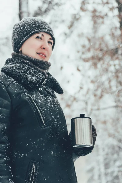 Портрет улыбающейся женщины с термостатом с горячим напитком, смотрящей на улицу и зимой — стоковое фото