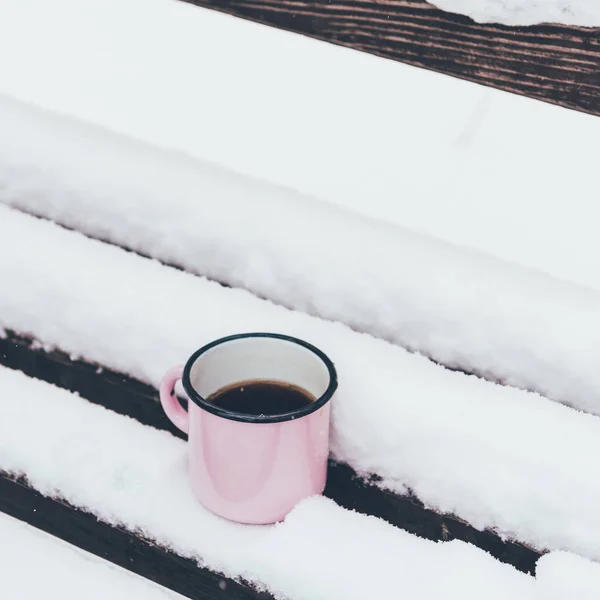Закрываем вид на чашечку кофе на деревянной скамейке в снежный день — стоковое фото
