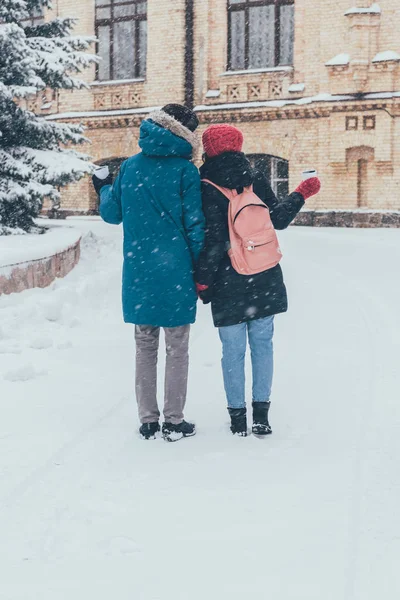 Rückansicht eines Paares mit Thermobechern, die sich im Winter an den Händen halten — Stockfoto