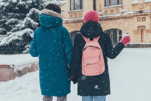 Back view of couple with thermocups holding hands in winter — Stock Photo